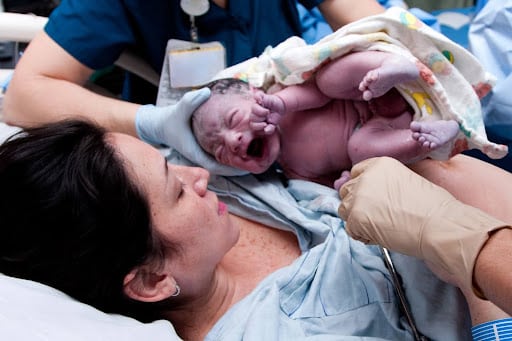 Nurse-handing-newborn-baby-to-mother-in-delivery-room-as-attendant-reaches-for-umbilical-cord-birth-injuries-compounded-by-medical-errors.jpg